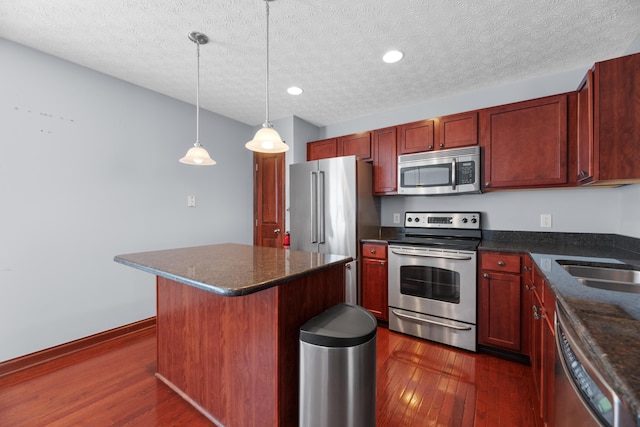 kitchen featuring a kitchen island, hanging light fixtures, appliances with stainless steel finishes, reddish brown cabinets, and dark wood-style floors