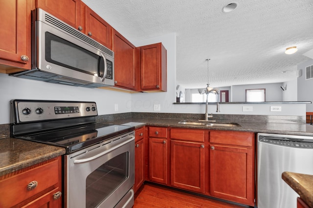 kitchen with dark wood-type flooring, a peninsula, stainless steel appliances, a textured ceiling, and a sink