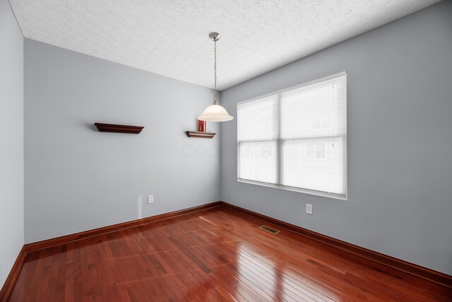 empty room with a textured ceiling, hardwood / wood-style floors, visible vents, and baseboards