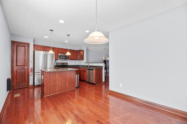 kitchen with dark wood finished floors, dark countertops, a center island, stainless steel appliances, and a sink
