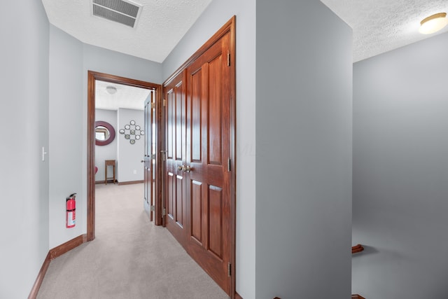 hallway featuring baseboards, visible vents, a textured ceiling, and light colored carpet