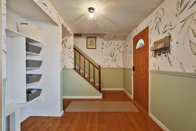 foyer entrance with baseboards, a textured ceiling, stairway, and wood finished floors