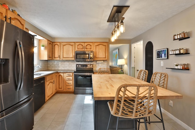 kitchen with backsplash, appliances with stainless steel finishes, light tile patterned flooring, a sink, and baseboards