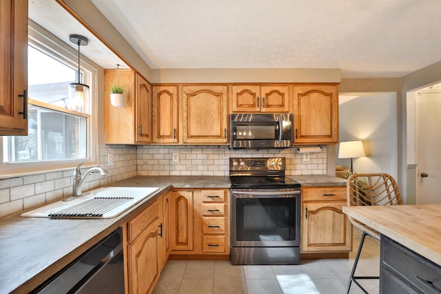 kitchen with light tile patterned floors, tasteful backsplash, stainless steel appliances, pendant lighting, and a sink