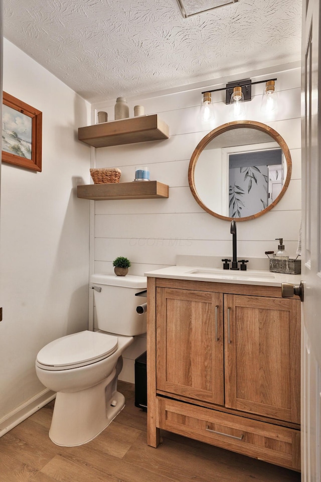 half bath with a textured ceiling, vanity, wood finished floors, and toilet