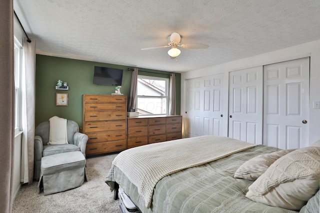 carpeted bedroom featuring ceiling fan, a textured ceiling, and two closets