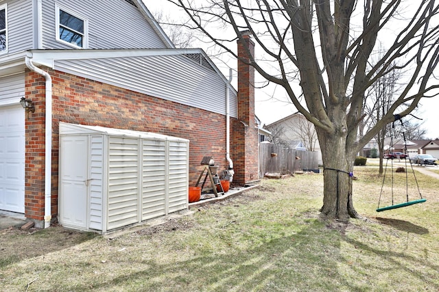 view of side of home featuring a garage, a yard, fence, and brick siding