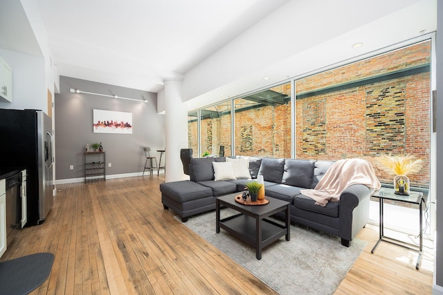 living room featuring brick wall, light wood-style flooring, and baseboards