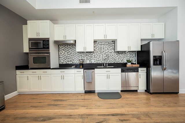 kitchen with stainless steel appliances, dark countertops, tasteful backsplash, a sink, and under cabinet range hood