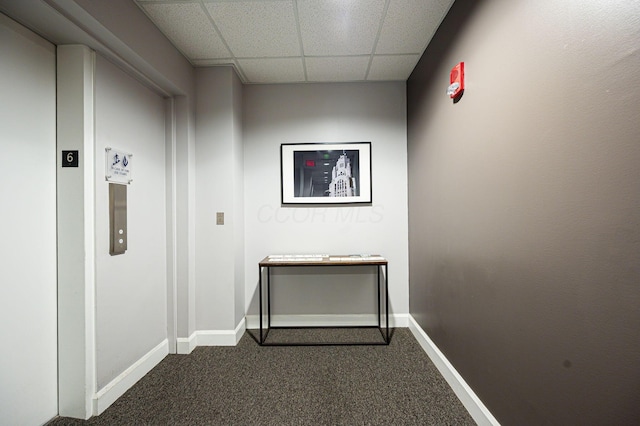 hall with baseboards, dark colored carpet, and a drop ceiling