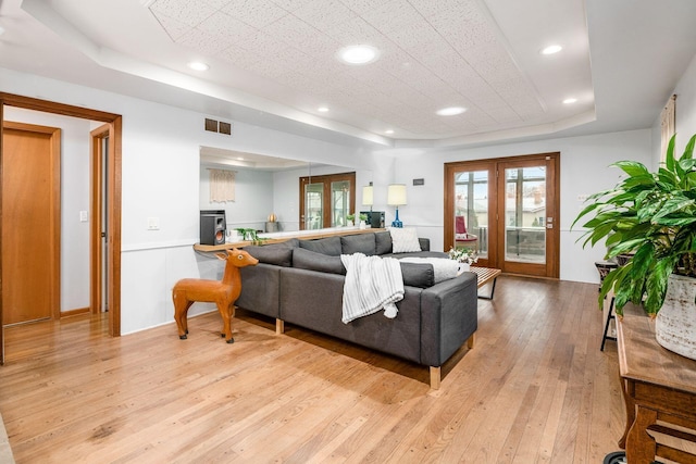 living room with visible vents, a tray ceiling, recessed lighting, french doors, and light wood-style floors