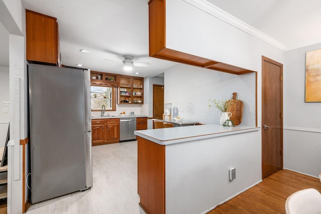 kitchen featuring a ceiling fan, a peninsula, a sink, appliances with stainless steel finishes, and brown cabinets