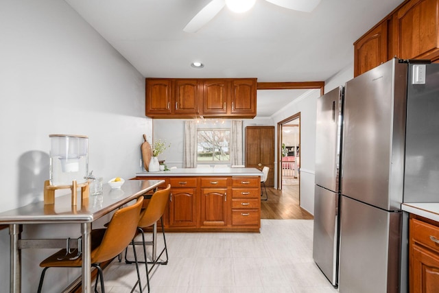 kitchen featuring ceiling fan, light countertops, recessed lighting, brown cabinets, and freestanding refrigerator