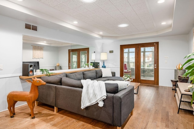 living room featuring visible vents, recessed lighting, french doors, light wood-style floors, and a raised ceiling