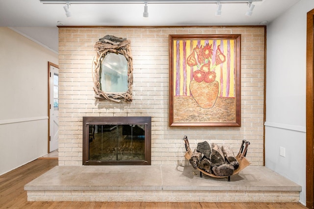 interior details with a brick fireplace, rail lighting, and wood finished floors