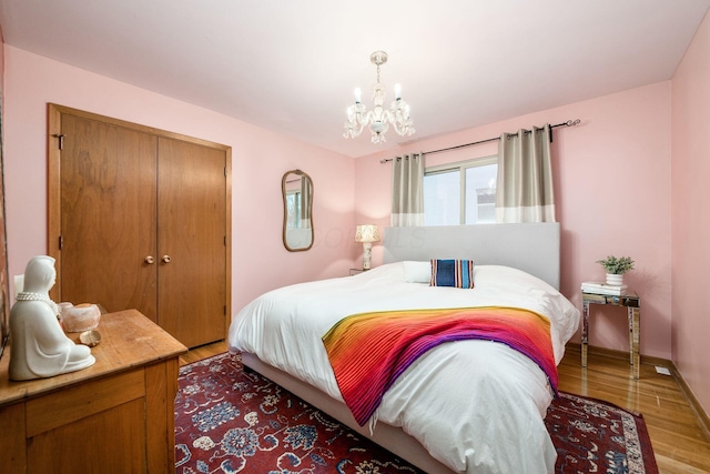 bedroom featuring an inviting chandelier, baseboards, light wood-type flooring, and a closet