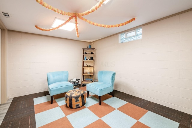 living area with tile patterned floors, visible vents, and concrete block wall