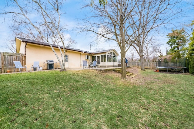 back of property with a trampoline, a yard, a sunroom, and stucco siding