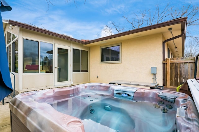 rear view of property featuring stucco siding, a hot tub, and fence