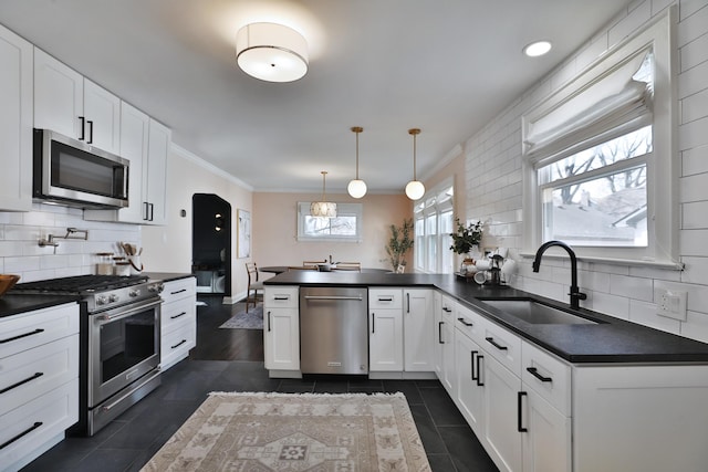 kitchen featuring a peninsula, appliances with stainless steel finishes, dark countertops, and a sink