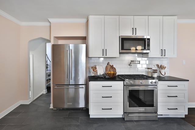 kitchen with tasteful backsplash, white cabinets, dark countertops, appliances with stainless steel finishes, and ornamental molding