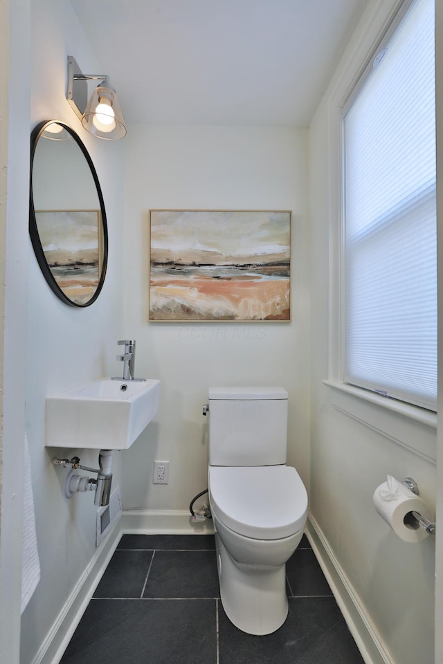 half bath with baseboards, toilet, and tile patterned floors