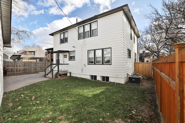 rear view of property with a lawn, a patio area, a fenced backyard, and central air condition unit