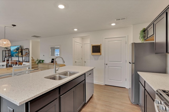 kitchen with a kitchen island with sink, a sink, visible vents, appliances with stainless steel finishes, and light stone countertops