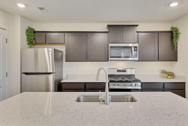 kitchen with light stone countertops, visible vents, stainless steel appliances, and a sink