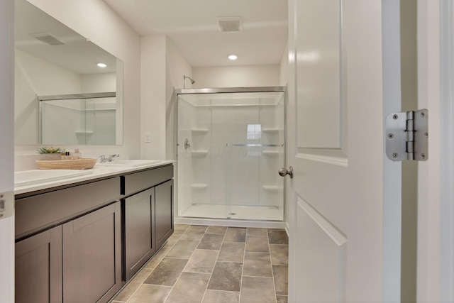 full bathroom with visible vents, a sink, a shower stall, and double vanity