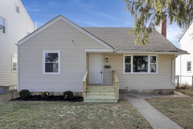 view of front of property featuring a chimney, a front lawn, and roof with shingles