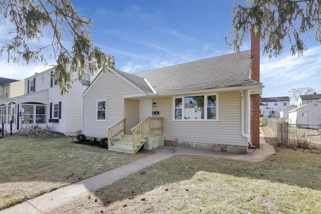 view of front facade featuring roof with shingles, a chimney, a sunroom, fence, and a front lawn