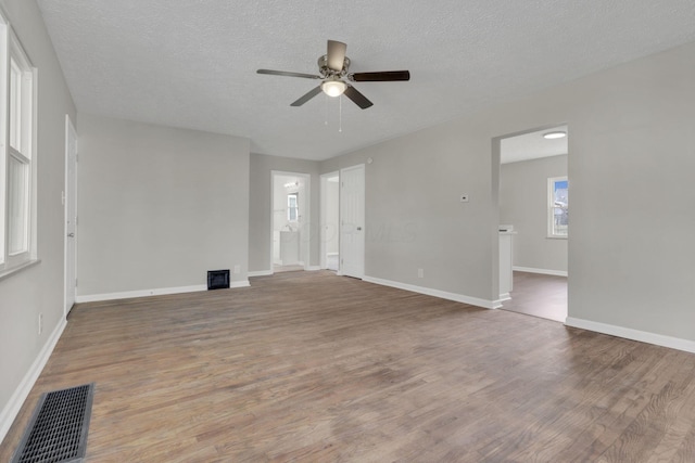 unfurnished living room with visible vents, a ceiling fan, a textured ceiling, wood finished floors, and baseboards