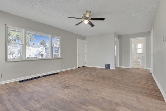 unfurnished living room with a textured ceiling, wood finished floors, visible vents, and baseboards