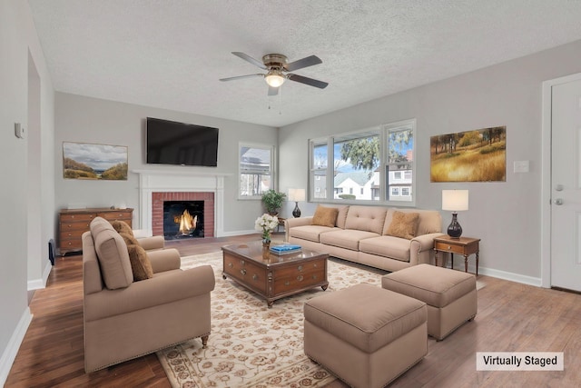 living area with a textured ceiling, a fireplace, wood finished floors, a ceiling fan, and baseboards