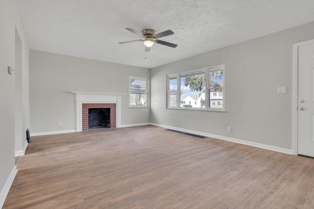 unfurnished living room with baseboards, ceiling fan, wood finished floors, a textured ceiling, and a brick fireplace