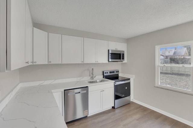 kitchen with white cabinets, light wood-style flooring, light stone countertops, stainless steel appliances, and a sink