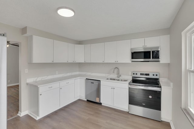 kitchen with light wood finished floors, light countertops, appliances with stainless steel finishes, white cabinetry, and a sink