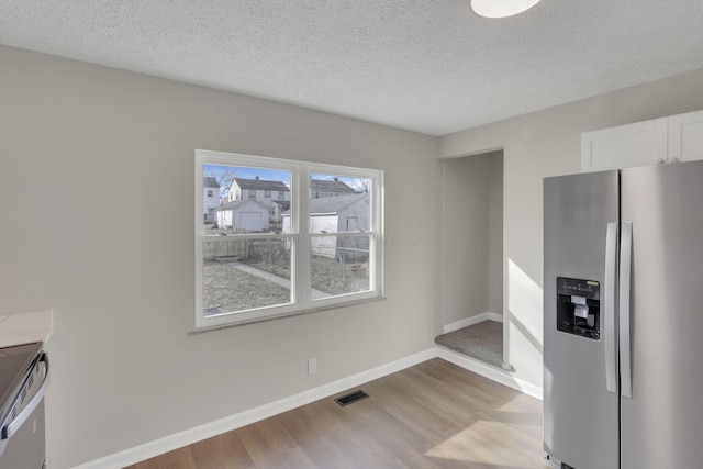 kitchen with a textured ceiling, stainless steel appliances, white cabinets, baseboards, and light wood-type flooring