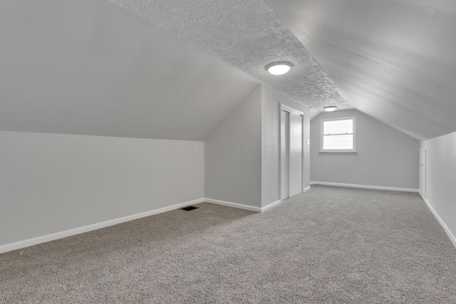 additional living space with carpet, baseboards, vaulted ceiling, and a textured ceiling