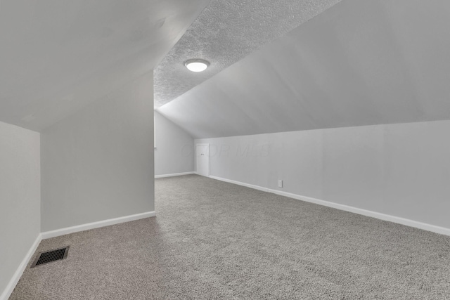 additional living space with baseboards, visible vents, a textured ceiling, and carpet flooring