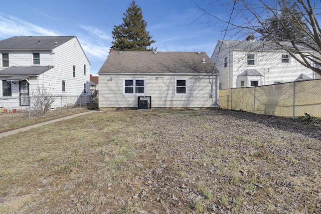 rear view of house with a shingled roof, a fenced backyard, and a lawn