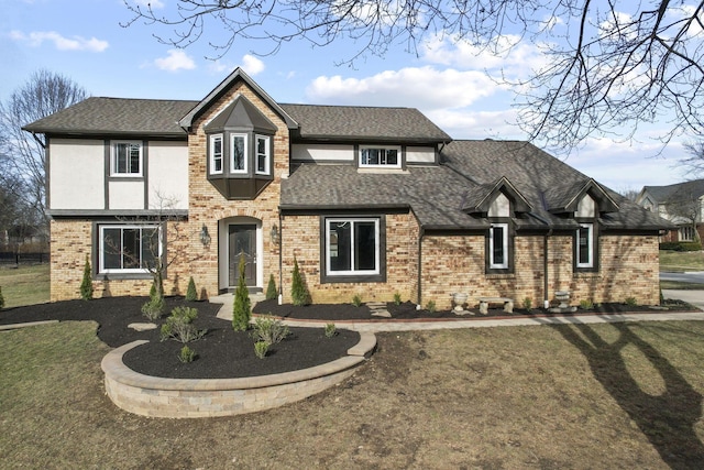 view of front of house with a shingled roof, a front yard, brick siding, and stucco siding