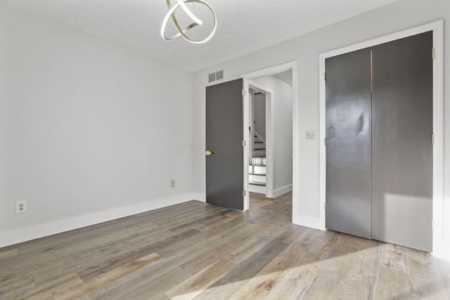 unfurnished bedroom featuring baseboards, a closet, visible vents, and wood finished floors