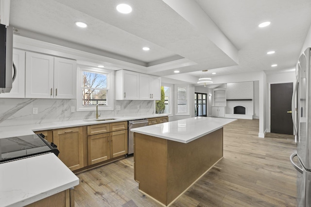 kitchen featuring a sink, appliances with stainless steel finishes, light wood-type flooring, a brick fireplace, and a tray ceiling