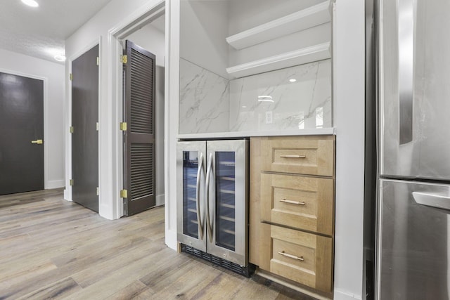 bar with a dry bar, light wood-style floors, and wine cooler