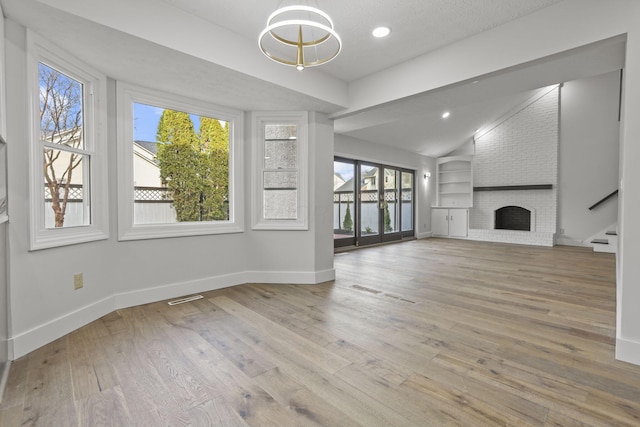 unfurnished living room with built in shelves, wood-type flooring, a brick fireplace, vaulted ceiling, and baseboards