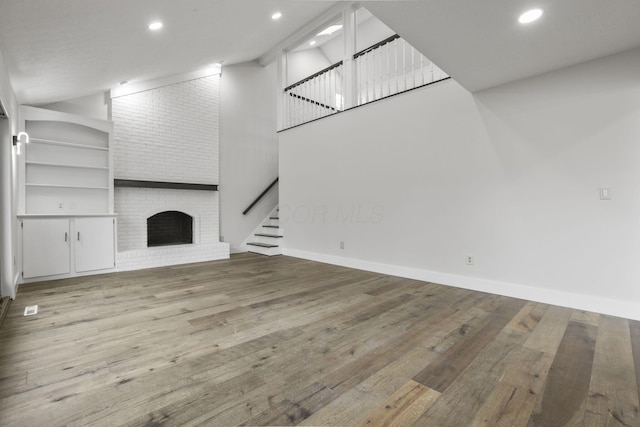 unfurnished living room featuring high vaulted ceiling, a brick fireplace, hardwood / wood-style flooring, and baseboards