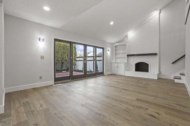 unfurnished living room featuring a brick fireplace, built in features, hardwood / wood-style floors, and french doors