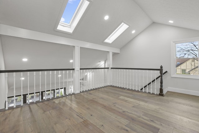 unfurnished room with vaulted ceiling with skylight, recessed lighting, wood finished floors, and baseboards